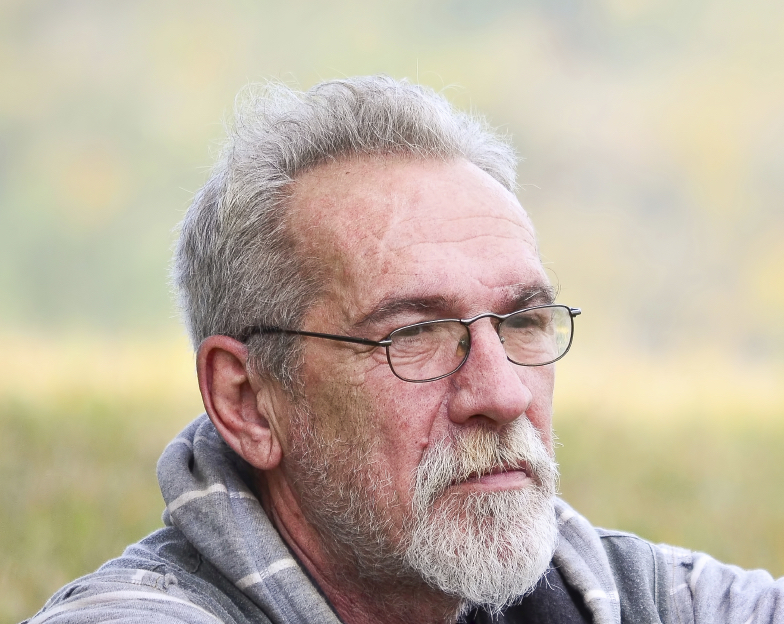 Portrait of an elderly, worried  man with a gray beard and glasses sitting on grass